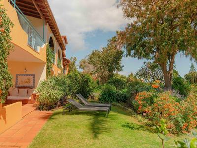 Wygodne leżaki w zielonym ogrodzie obok jasnego budynku pod niebieskim niebem.