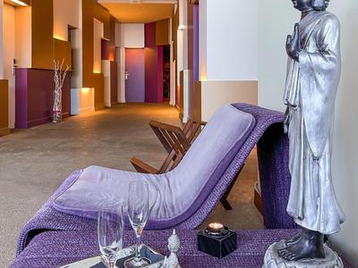 Hotelowy salon z fioletowym leżakiem, tacą, świecami i statuą Buddy w jasnym otoczeniu
