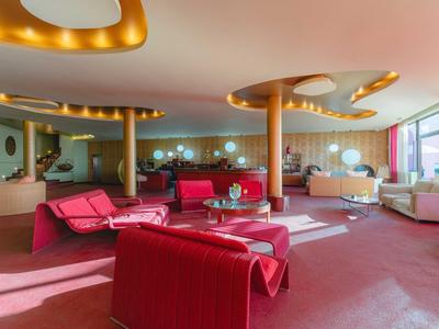 Nowoczesna hotelowa część wypoczynkowa z czerwonymi meblami i dużymi oknami.