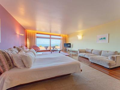 Jasny pokój hotelowy z dwoma łóżkami, sofą i dużym oknem z widokiem na morze.