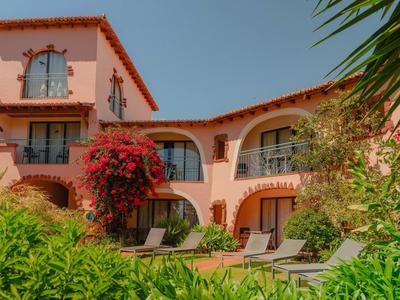 Hotel śródziemnomorski z czerwonymi kwiatami, leżakami przy basenie i czystym niebem.