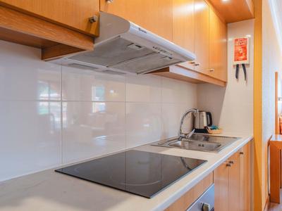 Nowoczesny aneks kuchenny z płytą indukcyjną, czajnikiem i drewnianymi szafkami w mieszkaniu.