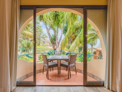 Balkon z stołem i krzesłami otoczony wysokimi zasłonami, z widokiem na palmy.