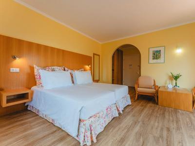 Jasny pokój hotelowy z podwójnym łóżkiem, drewnianą podłogą i przytulnym miejscem do siedzenia z dwoma fotelami.