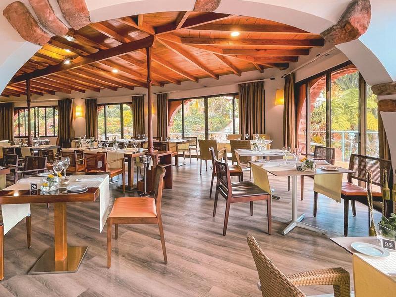 Jasna restauracja z drewnianymi belkami, dużymi oknami oraz nowoczesnymi stołami i krzesłami.