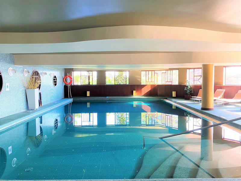 Jasny kryty basen z niebieskimi kafelkami, dużymi oknami i miejscem do siedzenia