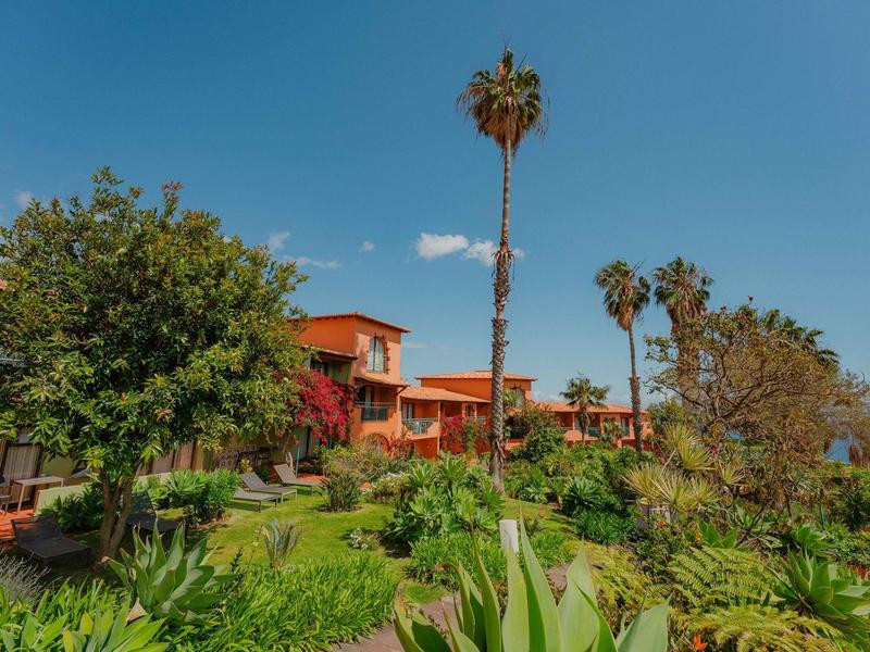 Budynek hotelu otoczony bujną zielenią i palmami pod niebieskim niebem