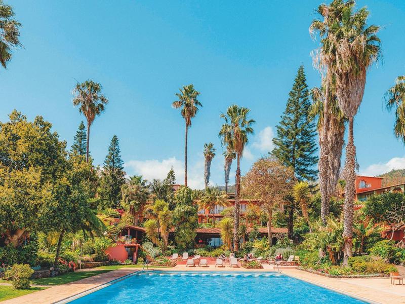 Basen otoczony zielonymi drzewami i palmami pod niebieskim niebem