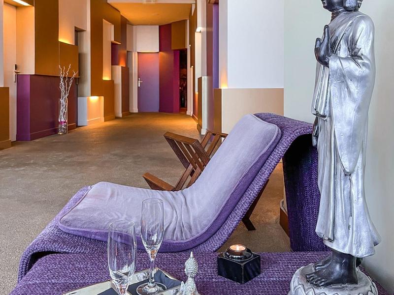 Hotelowy salon z fioletowym leżakiem, tacą, świecami i statuą Buddy w jasnym otoczeniu