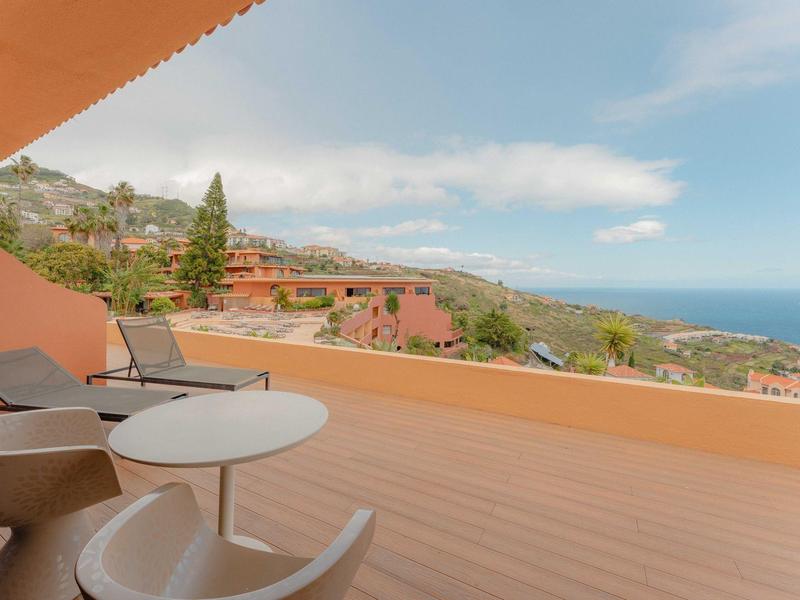 Balkon z stołami i krzesłami z widokiem na wybrzeże i zalesione wzgórza.