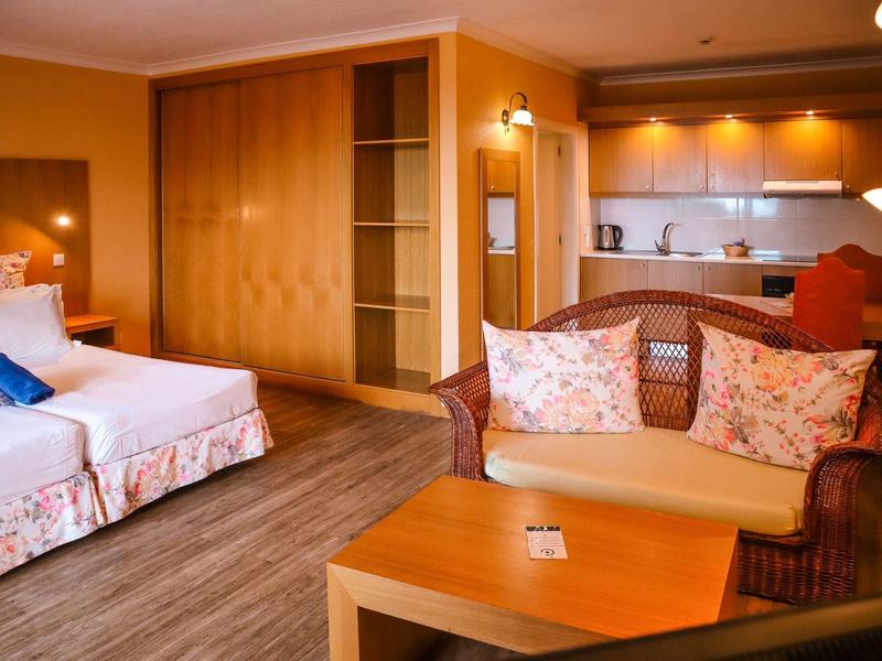 Przytulny pokój hotelowy z łóżkiem podwójnym, sofą, stolikiem kawowym i aneksem kuchennym.