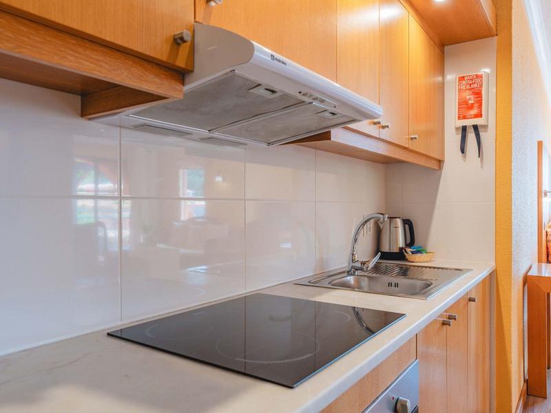 Nowoczesny aneks kuchenny z płytą indukcyjną, czajnikiem i drewnianymi szafkami w mieszkaniu.