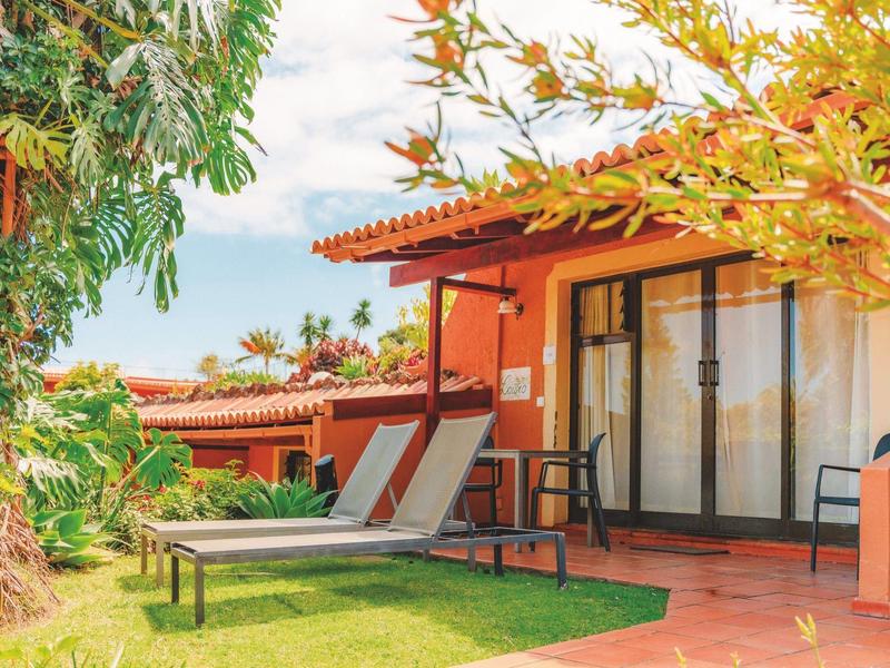 Wygodne leżaki przed tarasem pokoju hotelowego w otoczeniu zieleni.