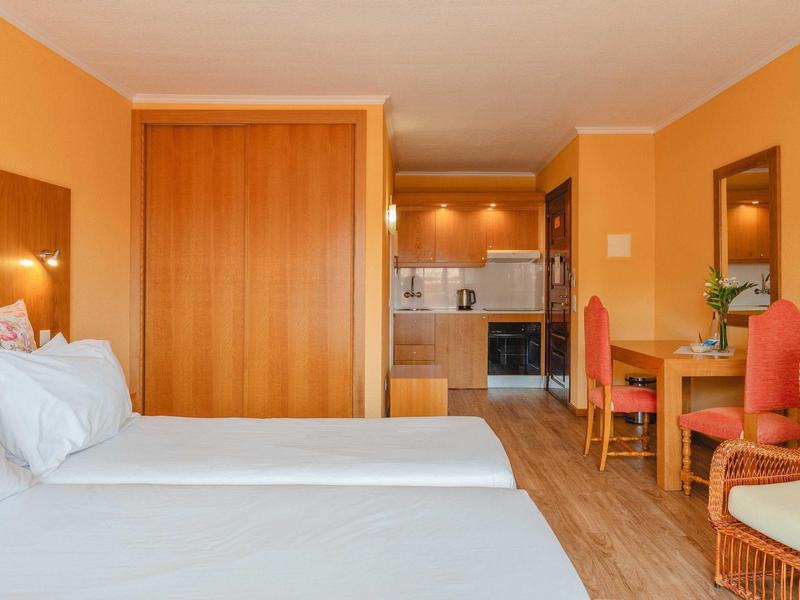 Jasno umeblowany pokój hotelowy z dwoma łóżkami, drewnianą podłogą i małym miejscem do pracy.