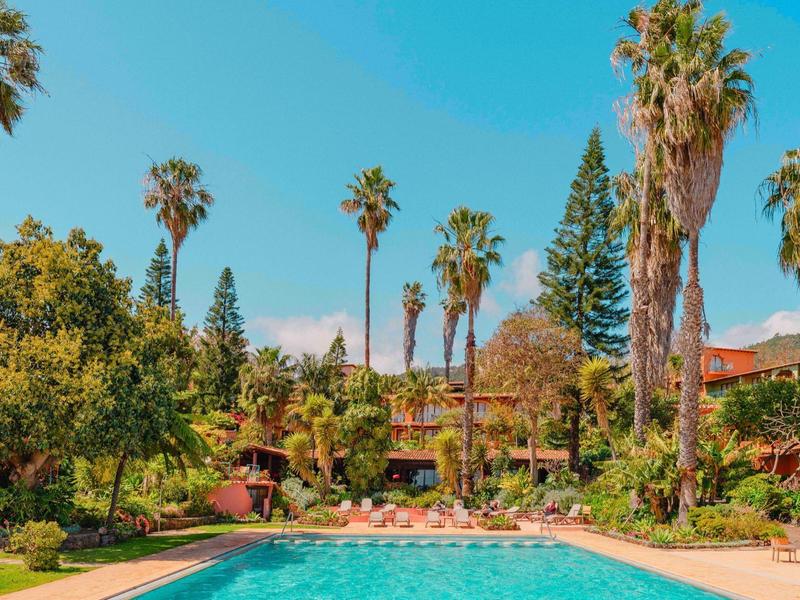 A pool surrounded by palm trees and lush vegetation under a clear blue sky.