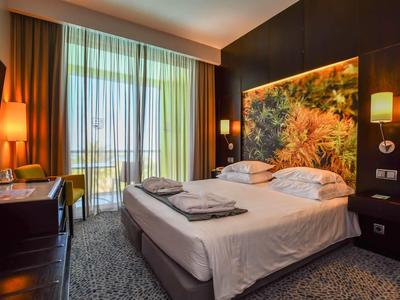 Chambre d'hôtel moderne avec lit double, balcon et éclairage chaleureux.