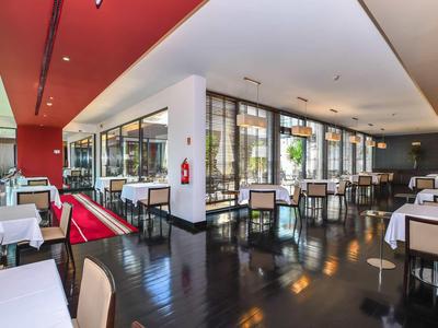 Restaurant moderne avec sols noirs, tables blanches et grandes fenêtres.