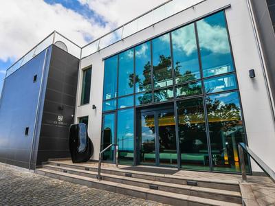 Hôtel moderne avec grande façade vitrée et escaliers à l'entrée sous un ciel bleu.