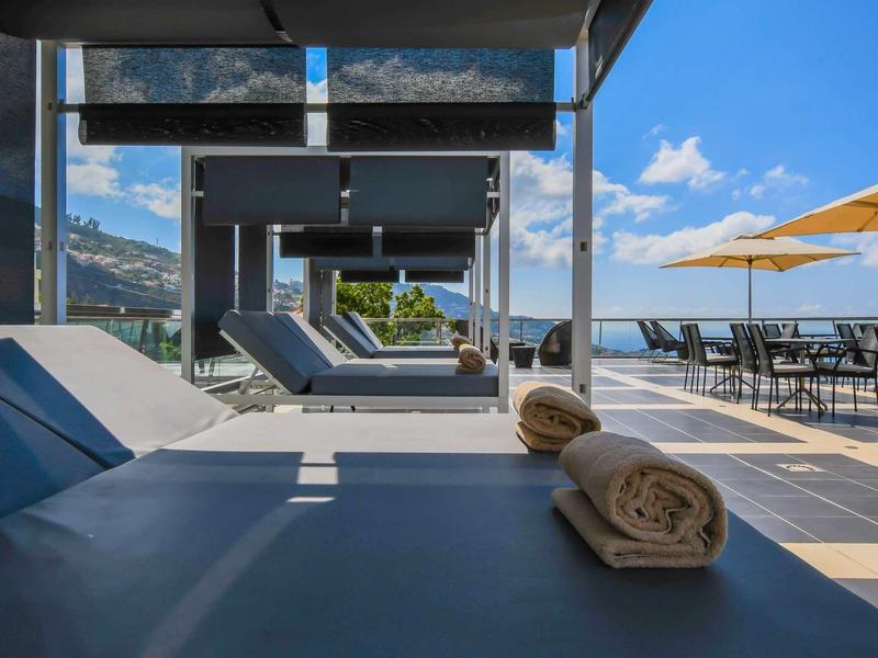Espace piscine extérieur moderne avec chaises longues et vue sur la mer sous un ciel bleu.