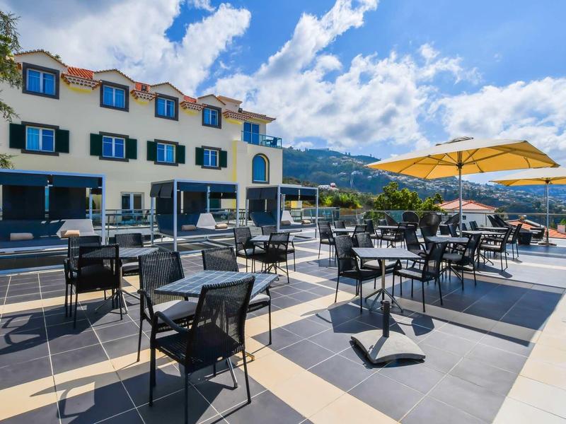 Espace extérieur d'hôtel avec tables, chaises et parasols par temps ensoleillé.