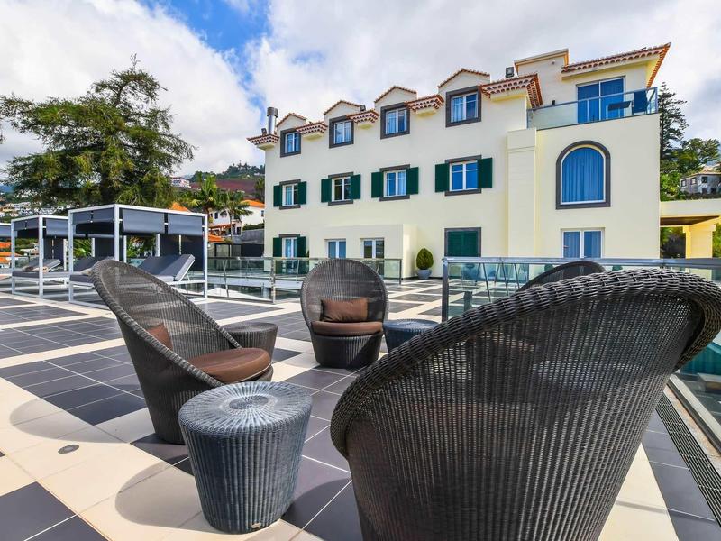 Terrasse moderne avec mobilier en osier noir devant un grand bâtiment hôtelier.