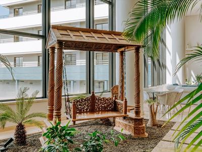 Traditional wooden bench swing in a bright indoor space with large windows and plants.