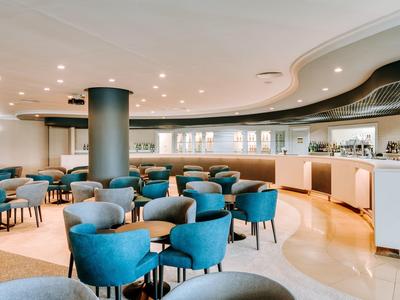Modern hotel restaurant with blue armchairs and a large bar in bright surroundings.