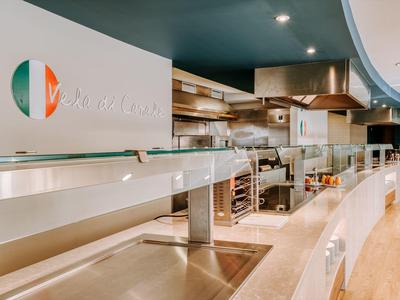 Modern hotel kitchen with stainless steel appliances and curved counter under indirect lighting.
