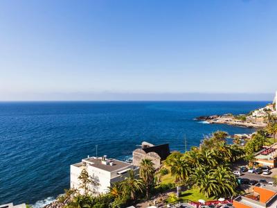 View of the sea with buildings, palm trees, and clear blue skies along the coast.