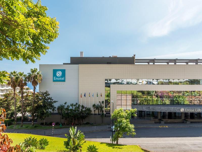 Modern hotel building with reflective glass facade and green front garden under blue sky