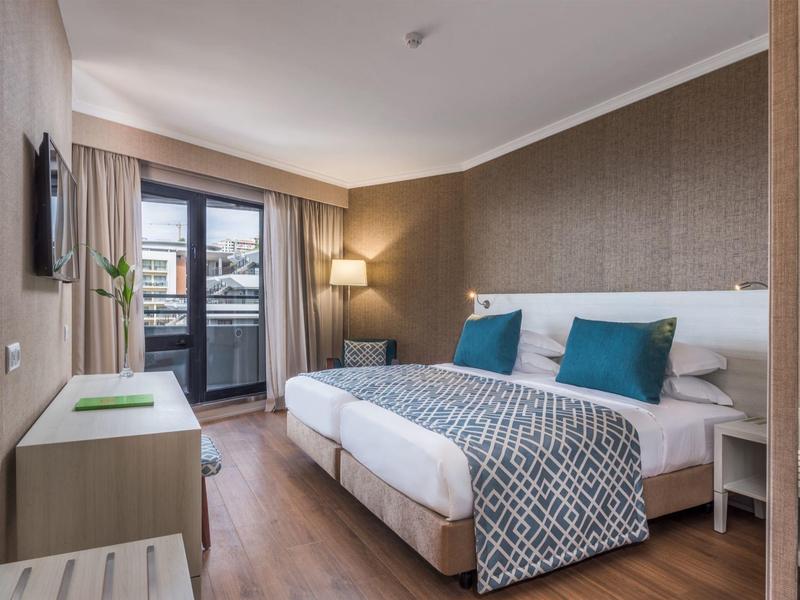 Modern hotel room with double bed, TV, and balcony with a view.