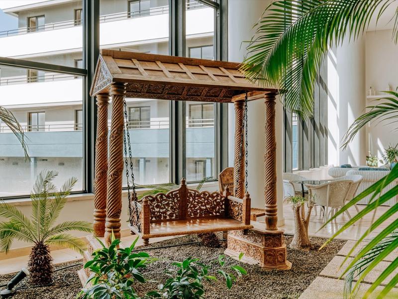 Traditional wooden bench swing in a bright indoor space with large windows and plants.