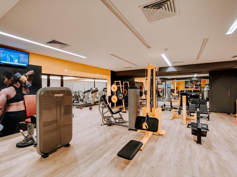 Modern gym with various workout equipment and light wooden flooring in a hotel.