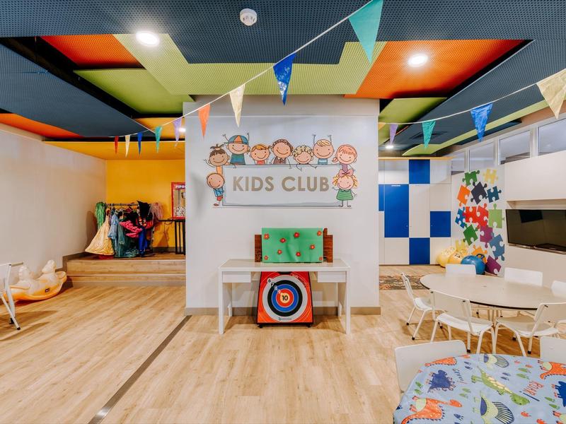 Colorful kids club room with seating platform, TV, and decorative flags on the ceiling.