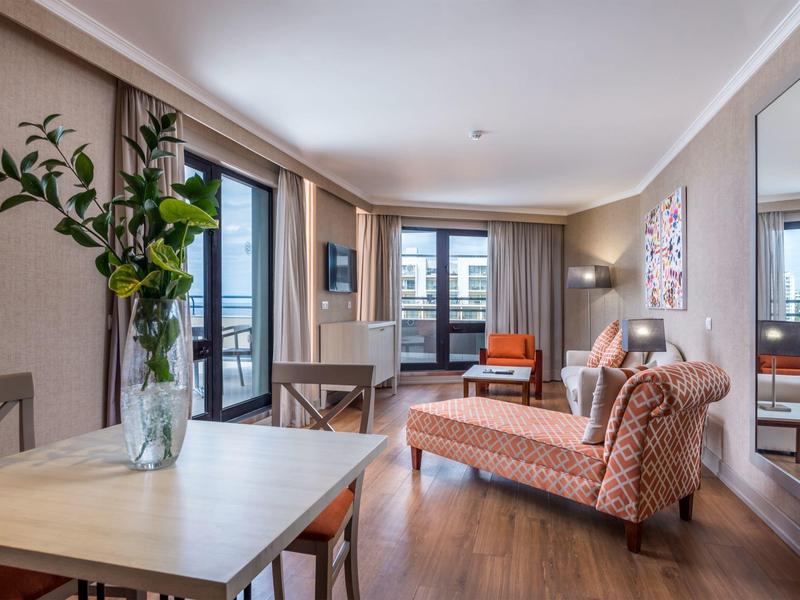 Modern living area with sofa, dining table, TV, and balcony with outdoor view.