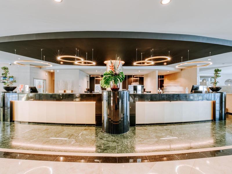 Modern hotel reception area with round desk, floral arrangement, and designer lighting.
