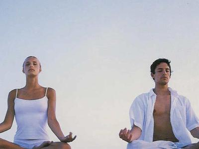 Un uomo e una donna meditano all'aperto in posizione del loto davanti a un cielo limpido.