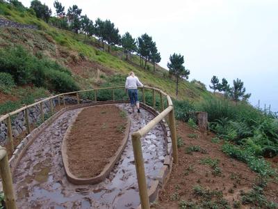 Person bearbeitet ein terrassiertes Feld an einem Berghang mit Geländer und Pflanzen.