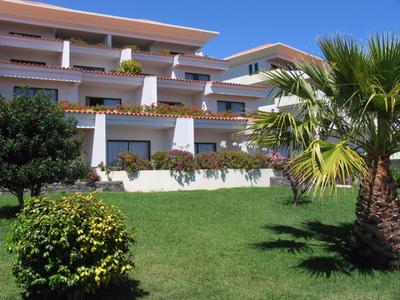 Complesso alberghiero moderno con giardino curato e palme sotto il sole.