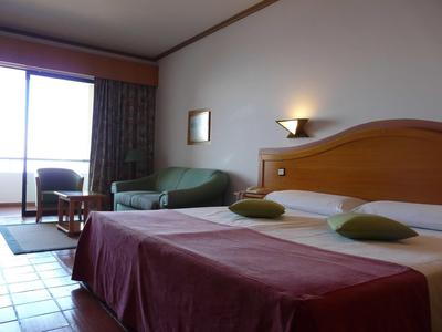 Camera d'hotel luminosa con letto matrimoniale, divano e balcone con vista mare.