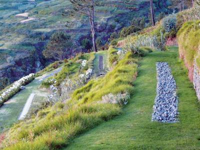 Paesaggio collinare verde con prato curato e sentieri decorativi in pietra.
