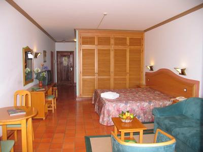 Camera d'hotel con letto matrimoniale, armadio in legno, scrivania, poltrona e terrazza con pavimento piastrellato.