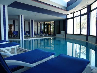 Piscina interna con lettini blu e ampie finestre in un hotel moderno.