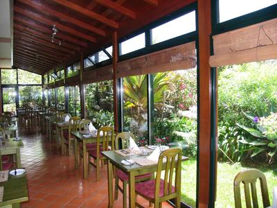 Ristorante con tavoli e sedie in legno, grandi finestre e vista sul giardino.