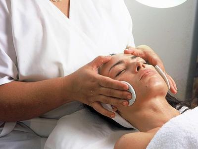 Un'estetista pulisce il viso di una cliente su un lettino sotto una luce intensa.