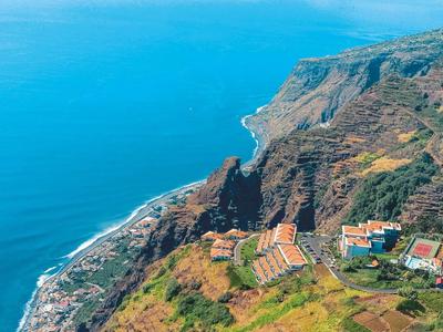 Paesaggio costiero con scogliere ripide, mare blu e villaggi su terreno collinare.