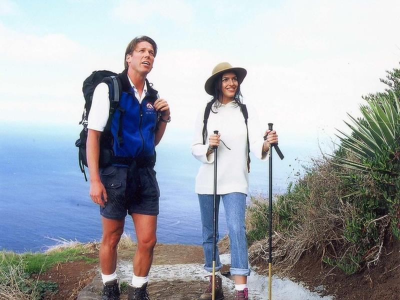 Due escursionisti con zaini e bastoncini da trekking su un sentiero con vista oceano.