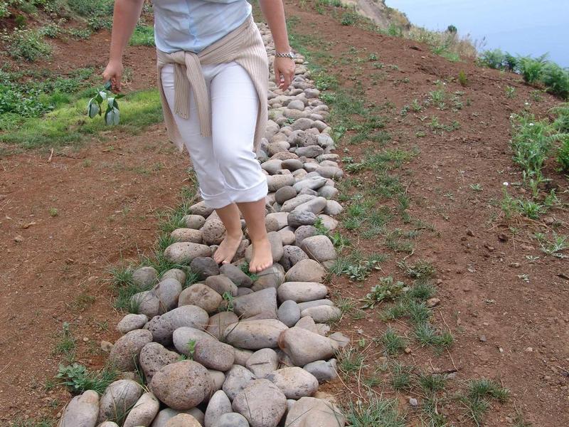Persona che cammina scalza su un sentiero di grandi pietre tra terra e erba.