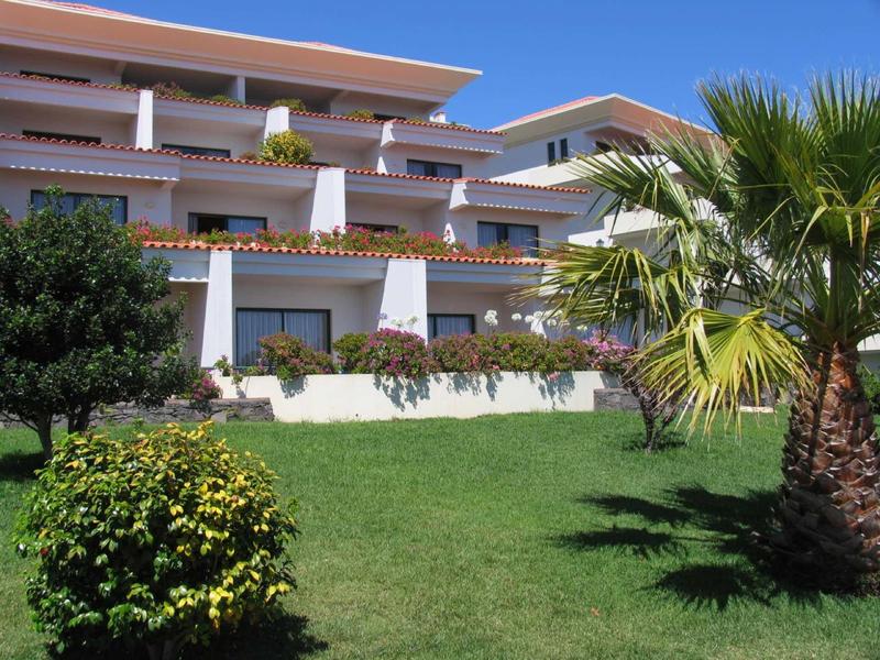 Complesso alberghiero moderno con giardino curato e palme sotto il sole.