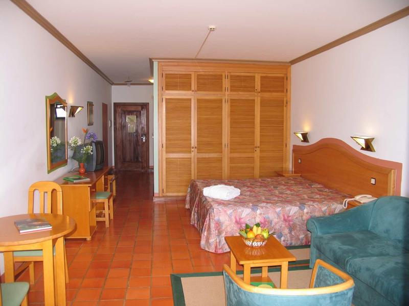 Camera d'hotel con letto matrimoniale, armadio in legno, scrivania, poltrona e terrazza con pavimento piastrellato.